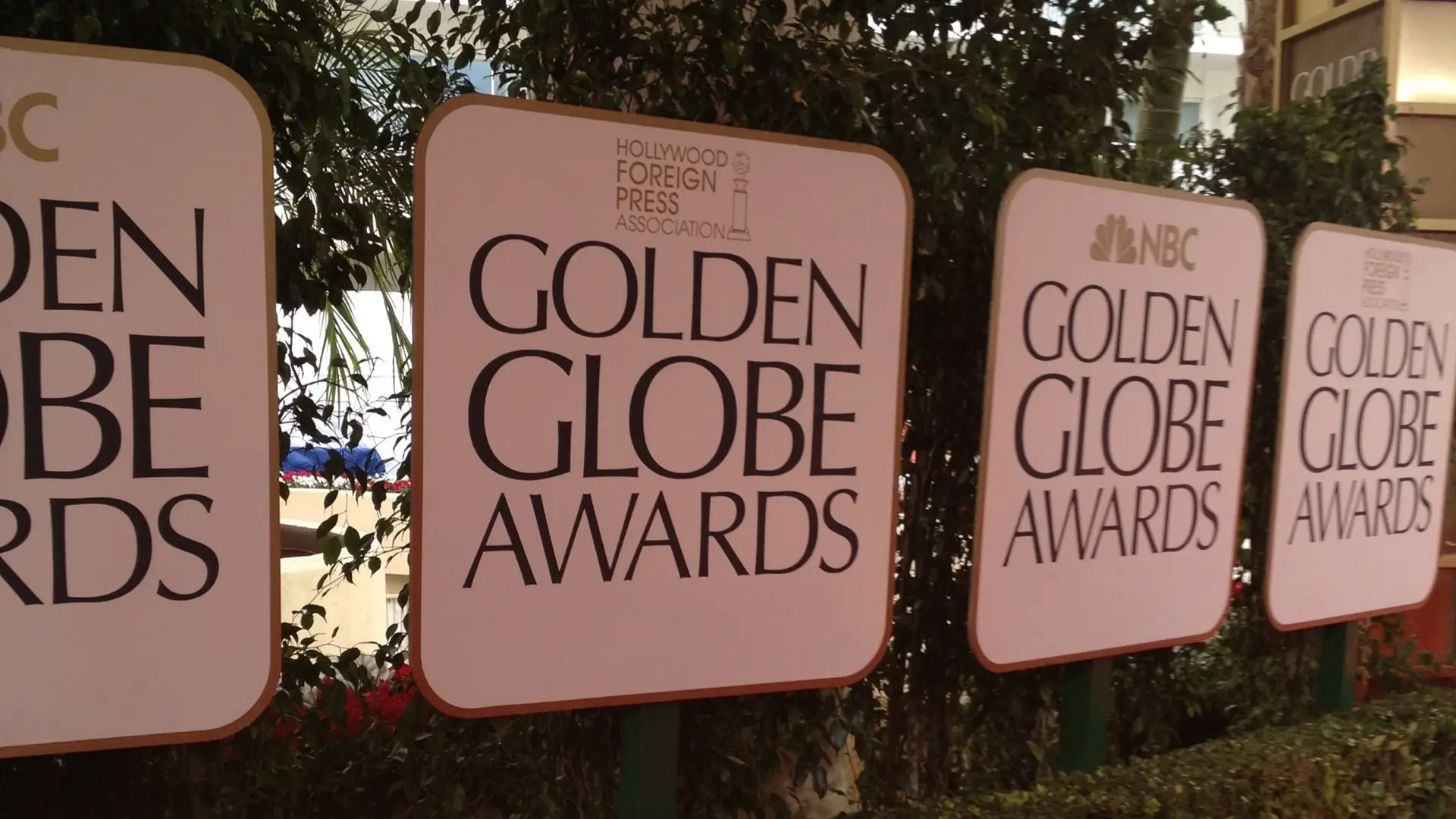 Banery Golden Globe Awards ustawione na zewnątrz podczas przygotowań do ceremonii, oficjalne logo Hollywood Foreign Press Association, tło z roślinnością.