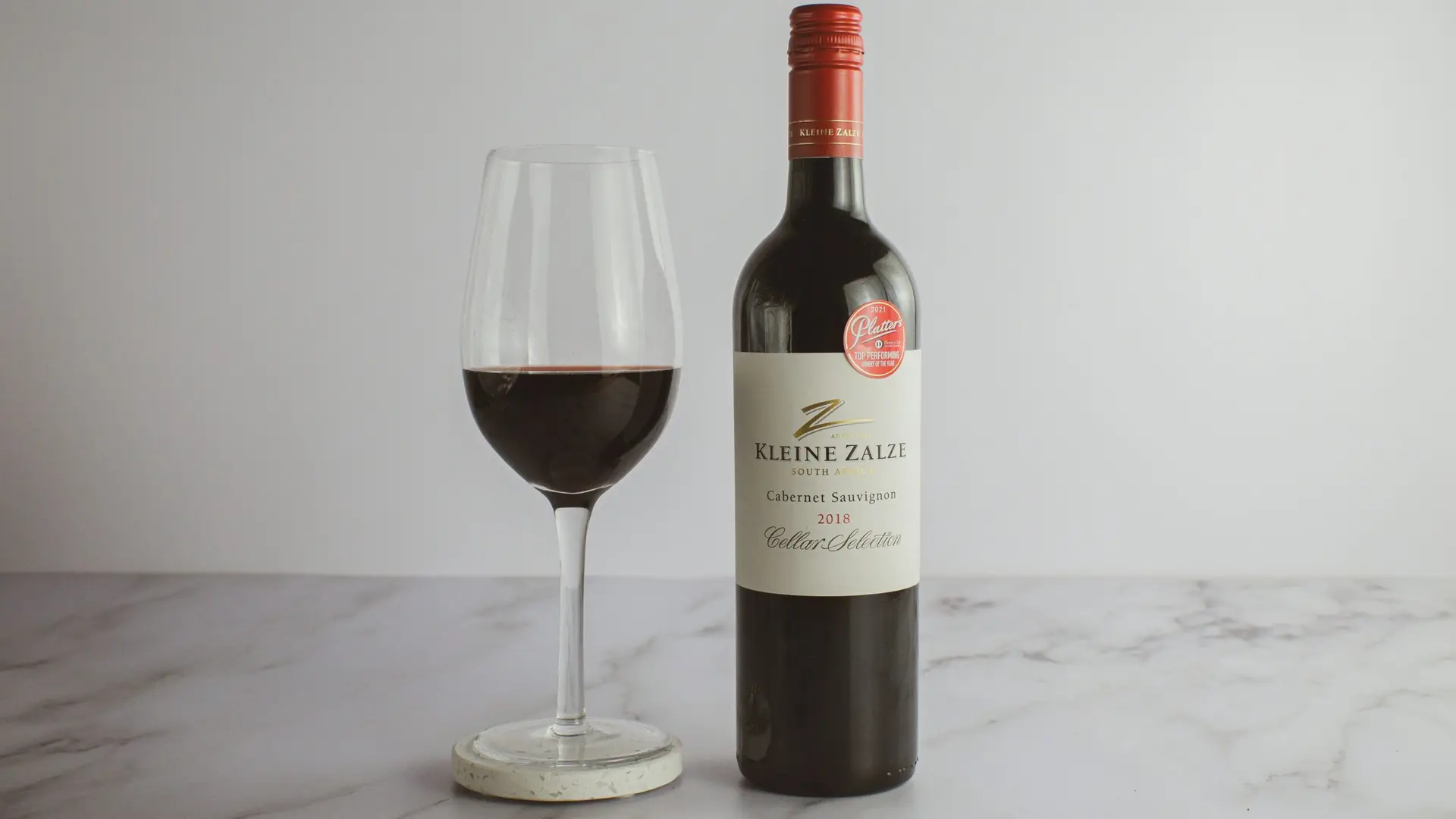 Butelka czerwonego wina Kleine Zalze Cabernet Sauvignon oraz kieliszek wina na jasnym tle