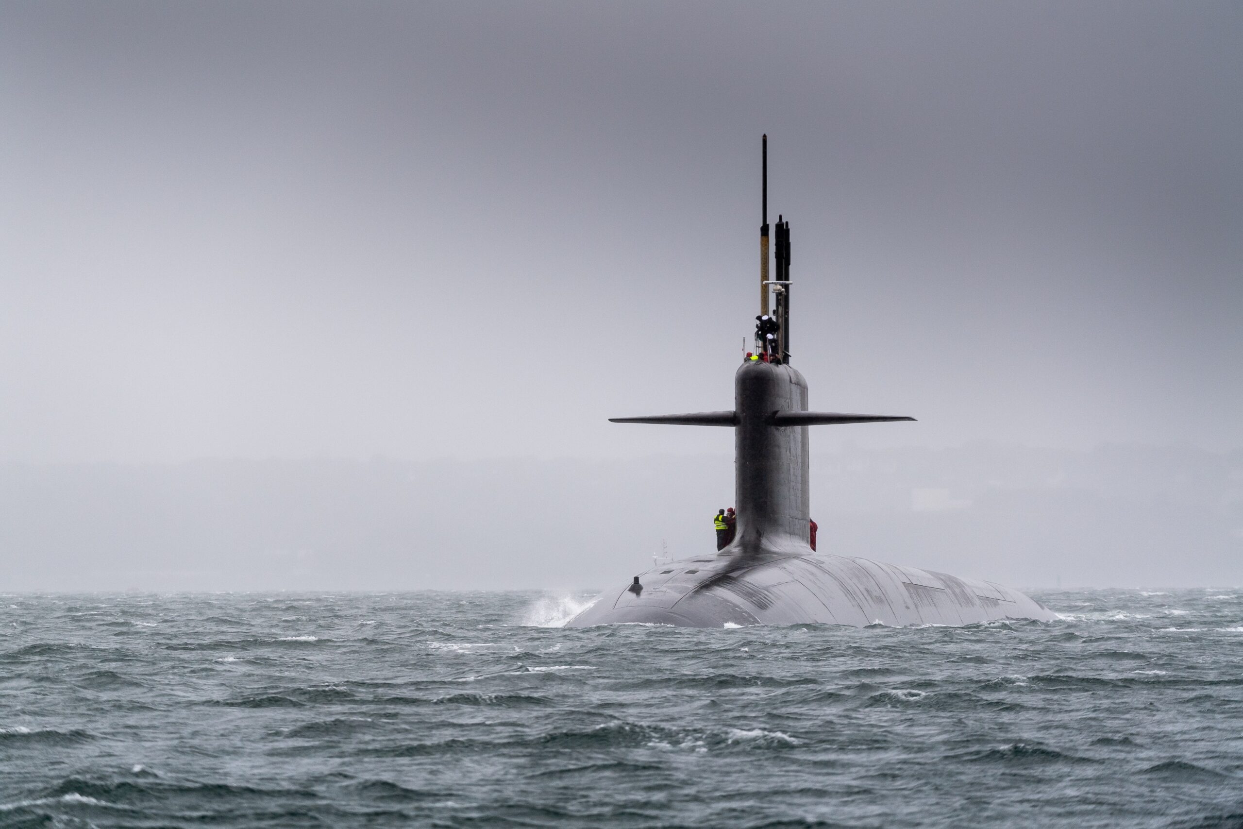 Francuski okręt podwodny o napędzie jądrowym wynurza się z wód Atlantyku w mglistych warunkach pogodowych. Na kiosku widoczni są marynarze.