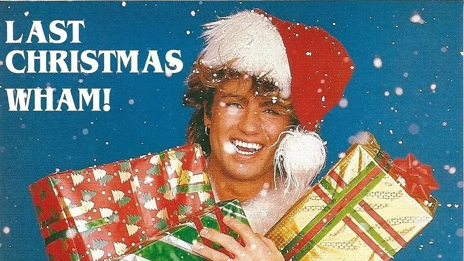 Świąteczna okładka singla ‘Last Christmas’ zespołu Wham!, przedstawiająca uśmiechniętą osobę w czapce Mikołaja trzymającą kolorowe prezenty na tle padającego śniegu.